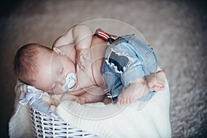 Newborn baby in jeans sleep in basket on floor