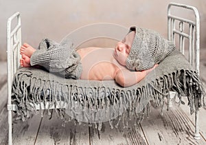 Newborn baby in knitted hat and pants sleeping on old cot