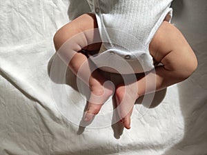 Newborn baby legs in white baby bodysuit, lying on white bed, warm light