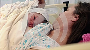 A newborn baby lies on the breast of a happy mother in the hospital. The first minutes of life.