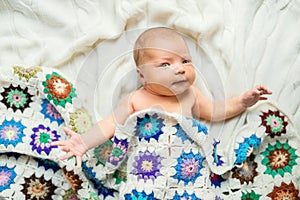 Newborn baby lying on bed, covered by a crocheted blanket. Top view.