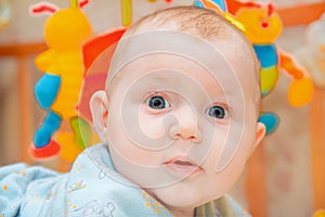 A newborn baby is lying in a children`s bed on the background of toys and smiling, close-up