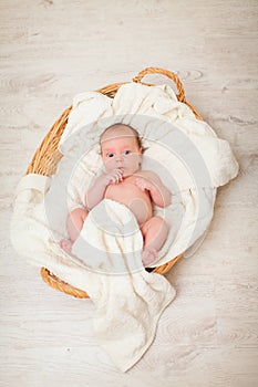 Newborn baby is lying in wicker basket. Basket on white wooden background. Newborn photo shoot