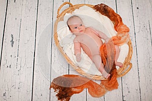 Newborn baby is lying in wicker basket. Basket on white wooden background. Newborn photo shoot