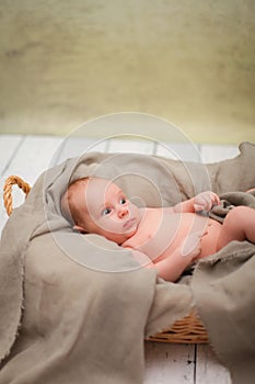 Newborn baby is lying in wicker basket. Basket on white wooden background. Newborn photo shoot