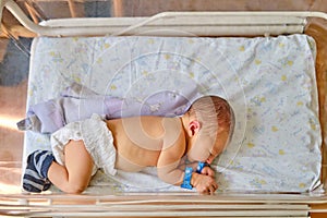 A newborn baby with a maternity hospital bracelet on his arm is sleeping in a crib. A newly born child in a clinic bed behind a