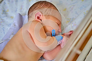 A newborn baby with a maternity hospital bracelet on his arm is sleeping in a crib. A newly born child in a clinic bed behind a