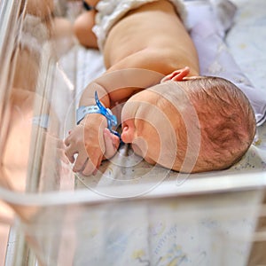 A newborn baby with a maternity hospital bracelet on his arm is sleeping in a crib. A newly born child in a clinic bed behind a