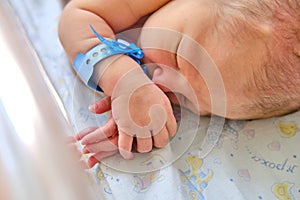 A newborn baby with a maternity hospital bracelet on his arm is sleeping in a crib. A newly born child in a clinic bed behind a