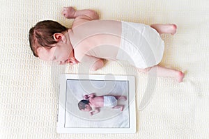 Newborn baby next to her photo on a tablet pc