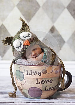 Newborn baby with owl hat in giant cup