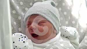 Newborn Baby Red Cute Face Portrait Early Days Crying In Medical Glass Bed On Grey Background. Child At Start Minutes Of