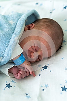 Newborn Baby Red Cute Face Portrait Early Days Sleeping In Medical Glass Bed On Blue Background. Child At Start Minutes