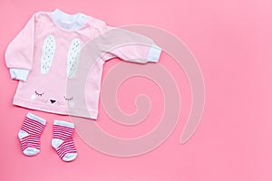 Newborn baby`s background. Clothes for small girl with booties on pink background top view copy space