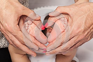 Newborn baby's feet in the hands of mom and dad, forming a heart