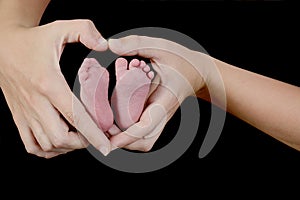 The newborn baby`s feet are in the heart-shaped hands of his mother. Focus on the foot and hands on the right.
