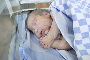 Newborn baby sleep in small hospital glass bed covered with blanket, arms crossed