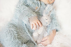 Newborn Baby. Sleeping Baby In Bed, Holding A Bunny Toy. Baby With Blue Knitted Romper