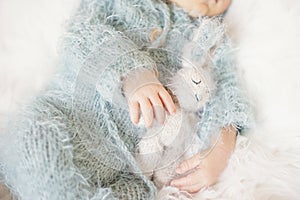Newborn Baby. Sleeping Baby In Bed, Holding A Bunny Toy. Baby With Blue Knitted Romper photo