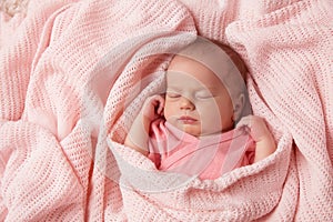 Newborn Baby sleeping in knitted Blanket. Cute Infant Child wrapped in Cotton Towel. New Born Little Girl resting in Pink Clothes
