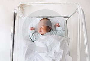 Newborn baby is sleeping in small transparent portable plastic bed.