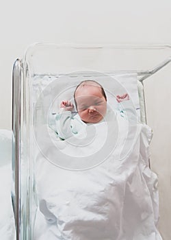 Newborn baby is sleeping in small transparent portable plastic bed.