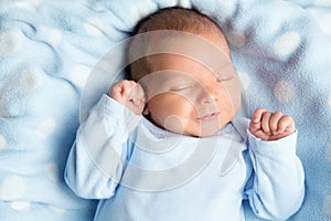 Newborn Baby Sleeping Smiling. Cute Infant Child in Wrap Bodysuit. New Born Little Boy smile in Blue Clothes lying on Blanket