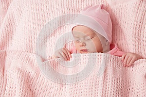 Newborn Baby sleeping under knitted Blanket. Cute Infant Child wrapped in Cotton Towel. New Born Little Girl resting in Pink