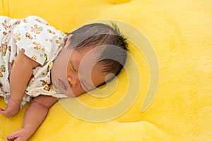 Newborn baby sleeping on yellow fur fabric bed.