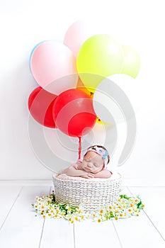 A newborn baby sleeps in a basket of daisies. A girl is flying in a hot air balloon.. A child with colorful balls.