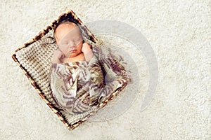 A newborn baby sleeps in a drawer wrapped in a knitted brown scarf on the white carpet