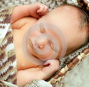 A newborn baby sleeps in a drawer wrapped in a knitted brown scarf on the white carpet