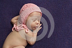 A newborn baby sleeps on a lilac plaid