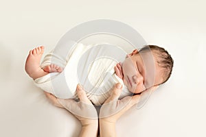 A newborn baby sleeps sweetly in his mother`s arms on a white background, swaddling the baby, a place for text