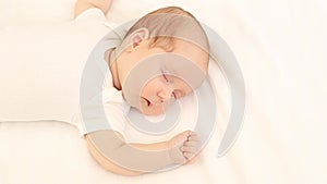 a newborn baby sleeps in a white bodysuit on a cotton bed at home, close-up portrait, space for text