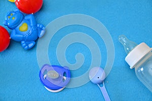 Newborn baby story. Children's toys, scissors, baby bottle, nipple, hairbrush on blue background. pacifier, toys