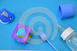 Newborn baby story. Children's toys, scissors, baby bottle, nipple, hairbrush on blue background. pacifier, toys