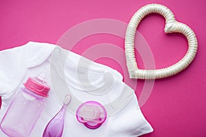 Newborn baby story. T-shirt and children's toys, scissors, baby bottle, nipple, hairbrush on red background