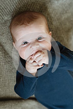 Newborn baby sucks hands in mouth, beautiful baby with blue eyes lies on  gray woolen plaid, gums itch, baby teething