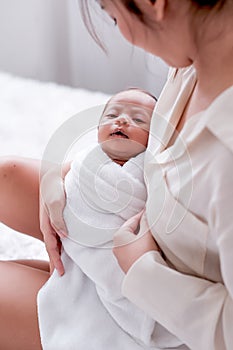 Newborn baby was held by her Asian mother who is sitting on the bed and look to baby face with love