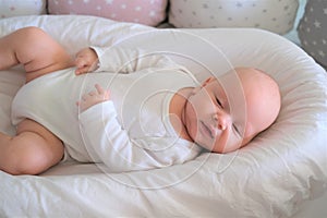 A newborn baby in white clothes lies on the bed. Portrait of a lying cute little child