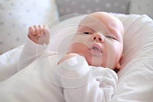 A newborn baby in white clothes lies on the bed. Portrait of a lying cute little child