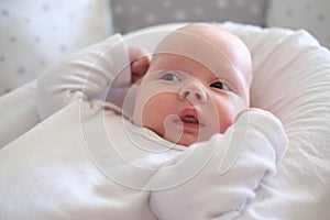 A newborn baby in white clothes lies on the bed. Portrait of a lying cute little child