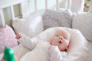 A newborn baby in white clothes lies on the bed. Portrait of a lying cute little child