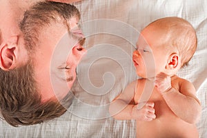 Newborn on the bed with his father close-up. The concept of the relationship of children and parents from birth.