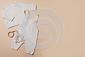 Newborn beige romper, sweater, pants, shoes, wooden toys on neutral backgroundd. Set of knitted baby clothes. Top view