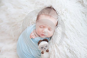 A newborn in a blue cocoon sleeps on a white blanket with pile, a child with a toy