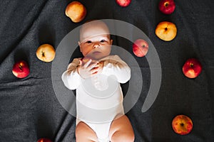 Newborn boy lying with apples. A small child in a white bodysuit