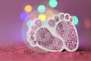 Newborn card.The birth of a girl. Pink glitter decorative baby feet on pink glitter background with yellow multicolored