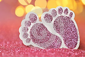 Newborn card.The birth of a girl. Pink glitter decorative baby feet on pink glitter background with yellow multicolored